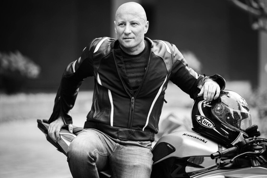 Biker sitting on a motorcycle in black and white, wearing a leather jacket.